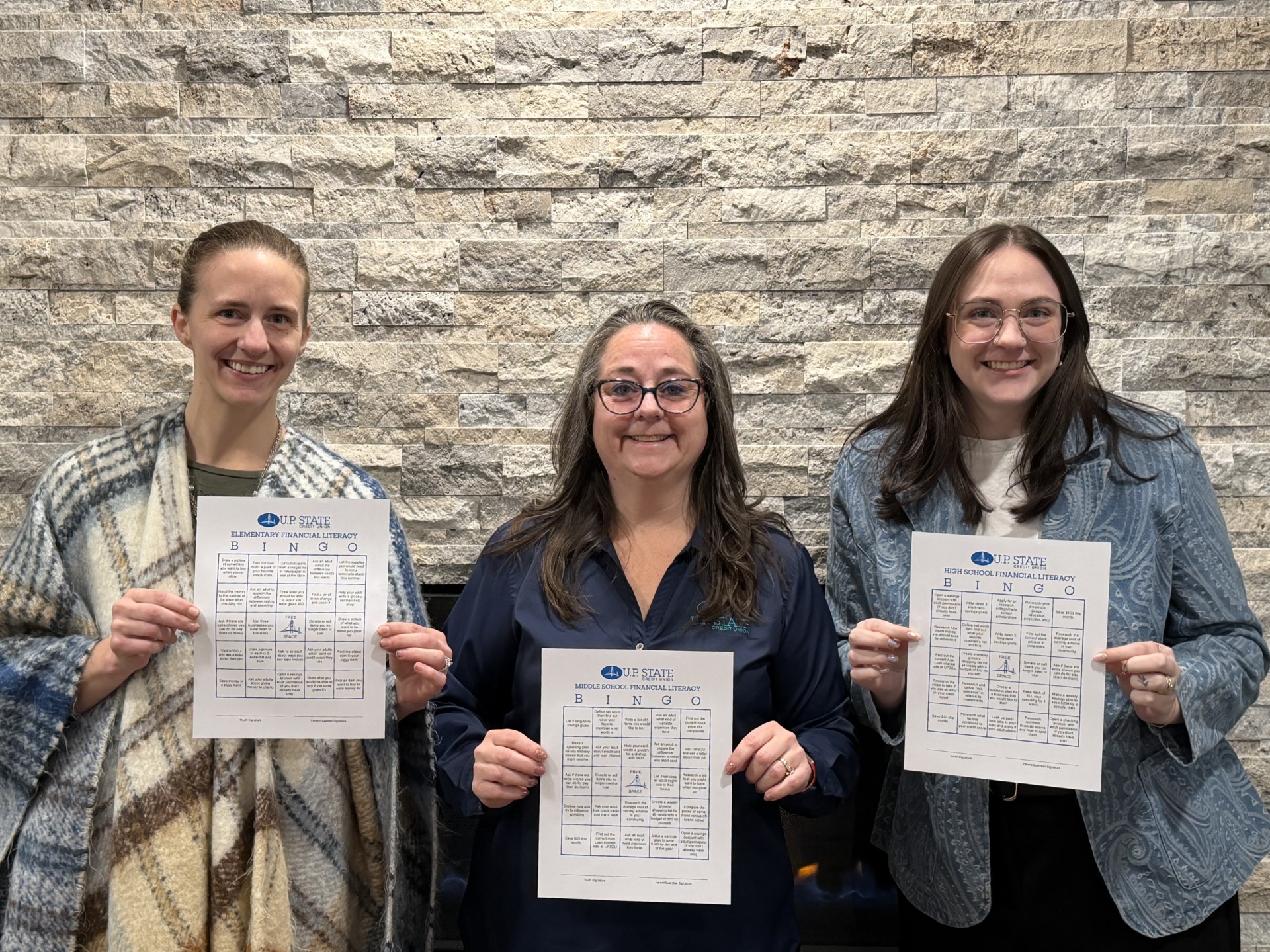 Jennifer, Theresa, and Kenadie from the Escanaba branch showcase the bingo cards for each age group.